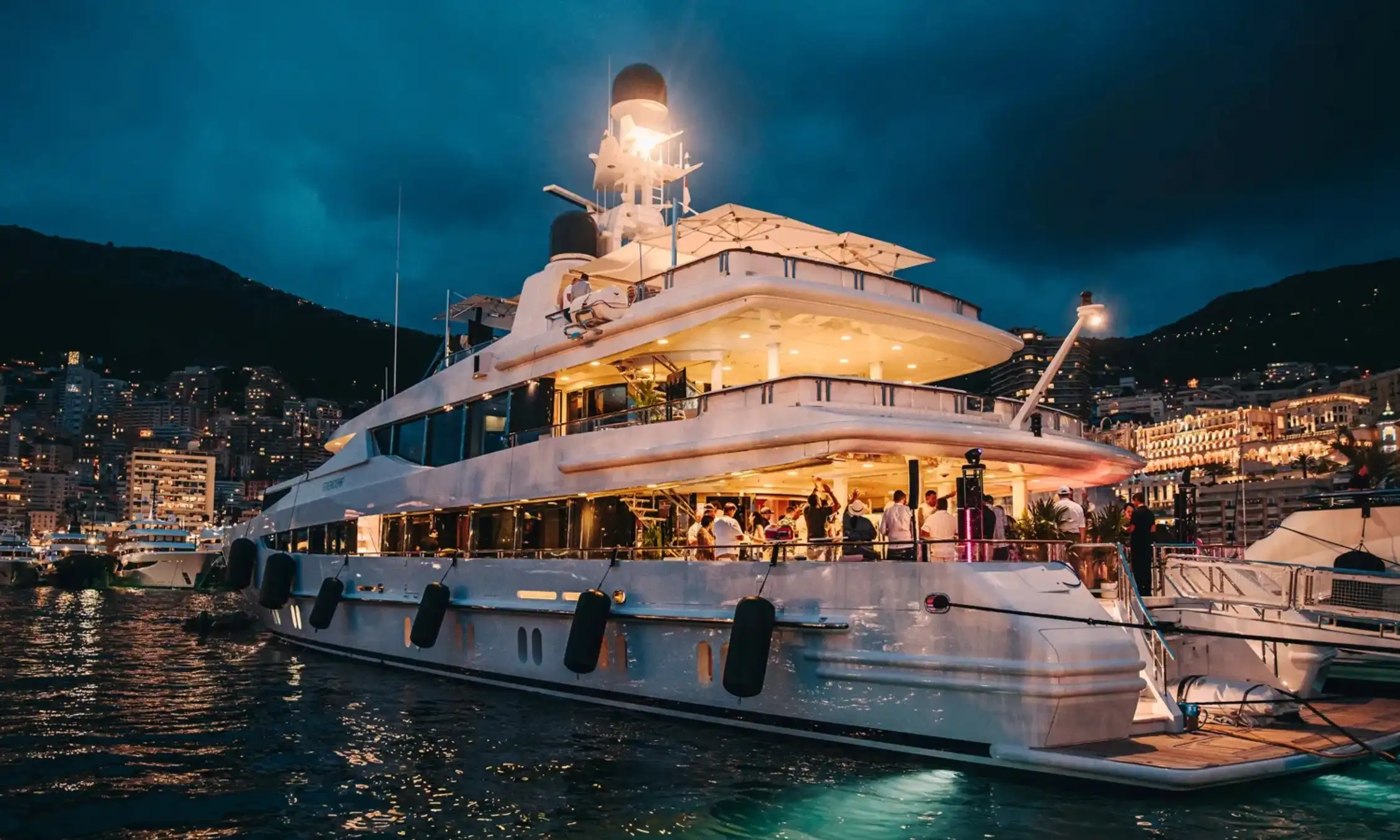 Evening scene showing illuminated yachts in Monaco harbour.