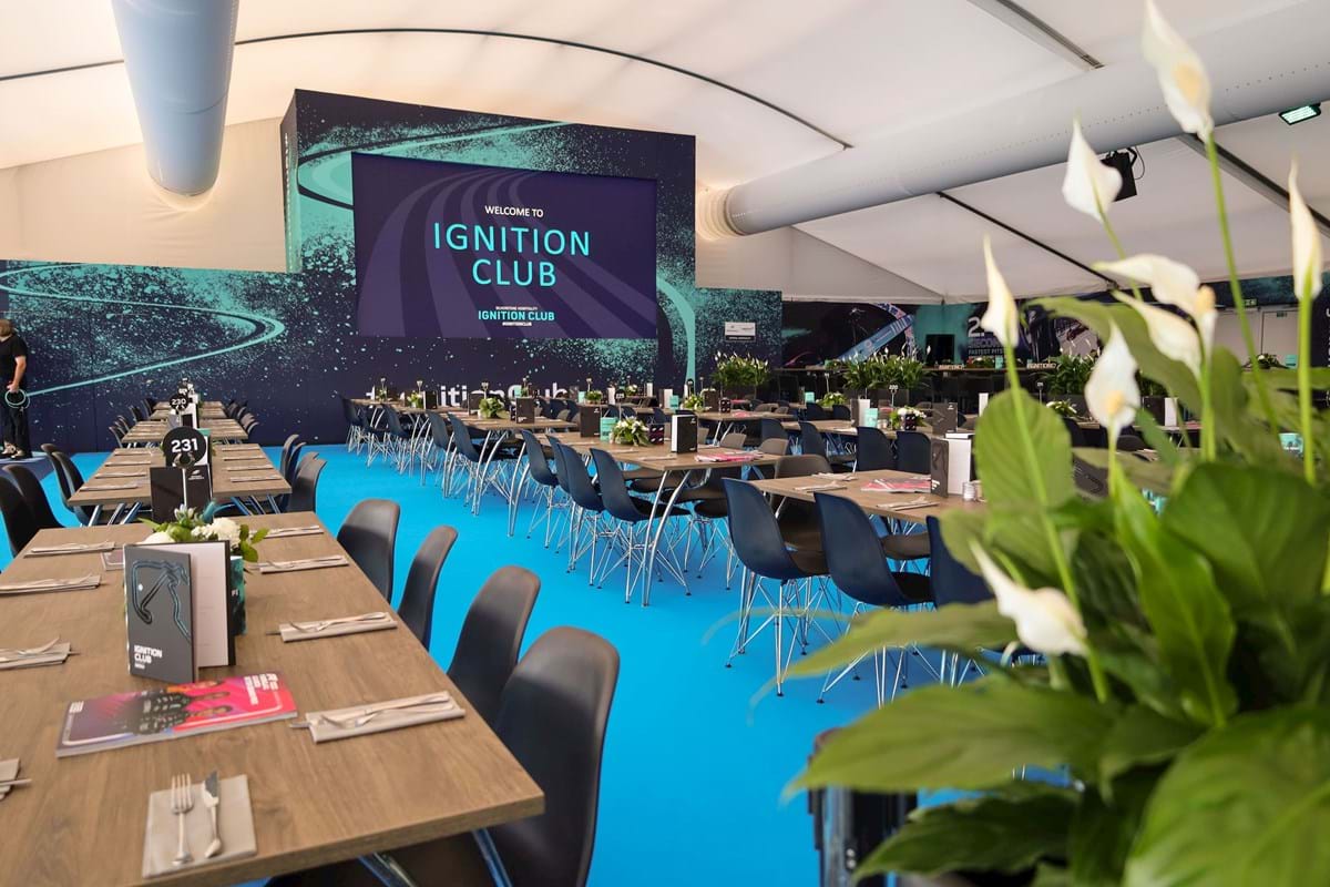 Interior of a licensed VIP suite like the Ignition Club or Pegasus Lounge, with panoramic views of the Silverstone track during the British Grand Prix.